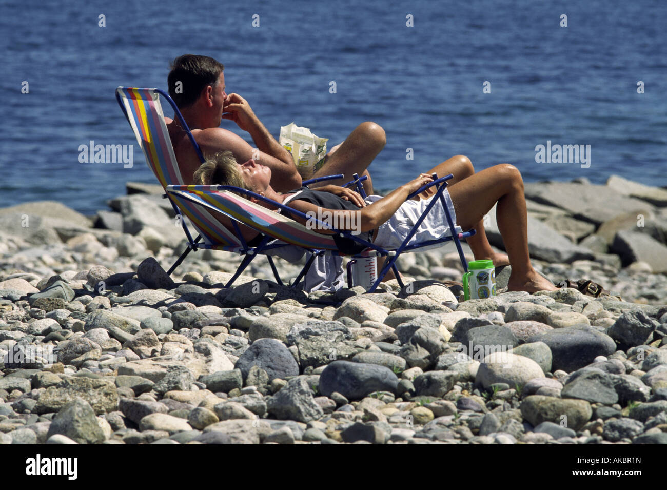A couple suns themselves on a rocky beach in Scituate Massachusetts Stock Photo
