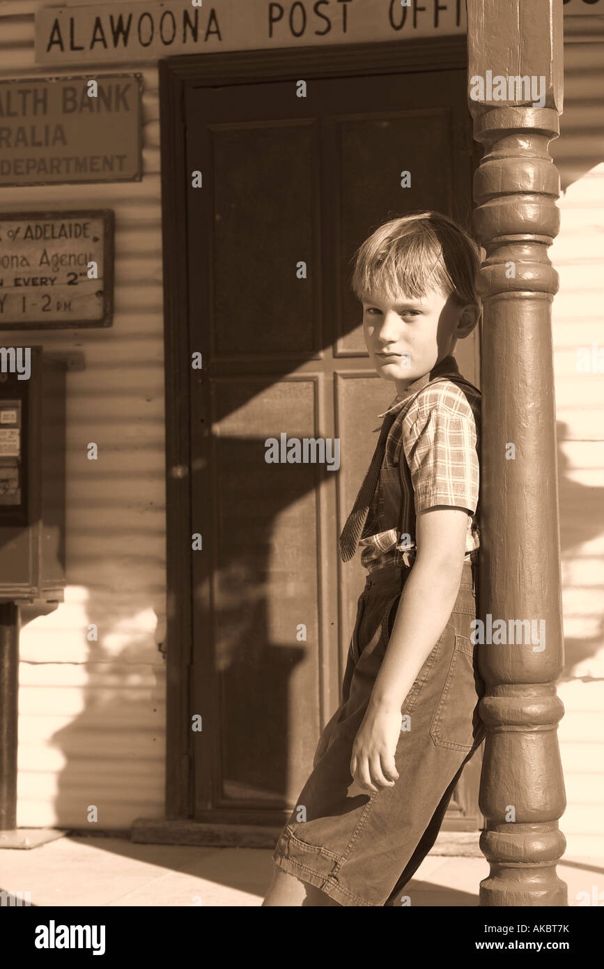 old style silver gelatin image of a boy in appropriate dress leaning a against a pole shop signage is fictitious Stock Photo