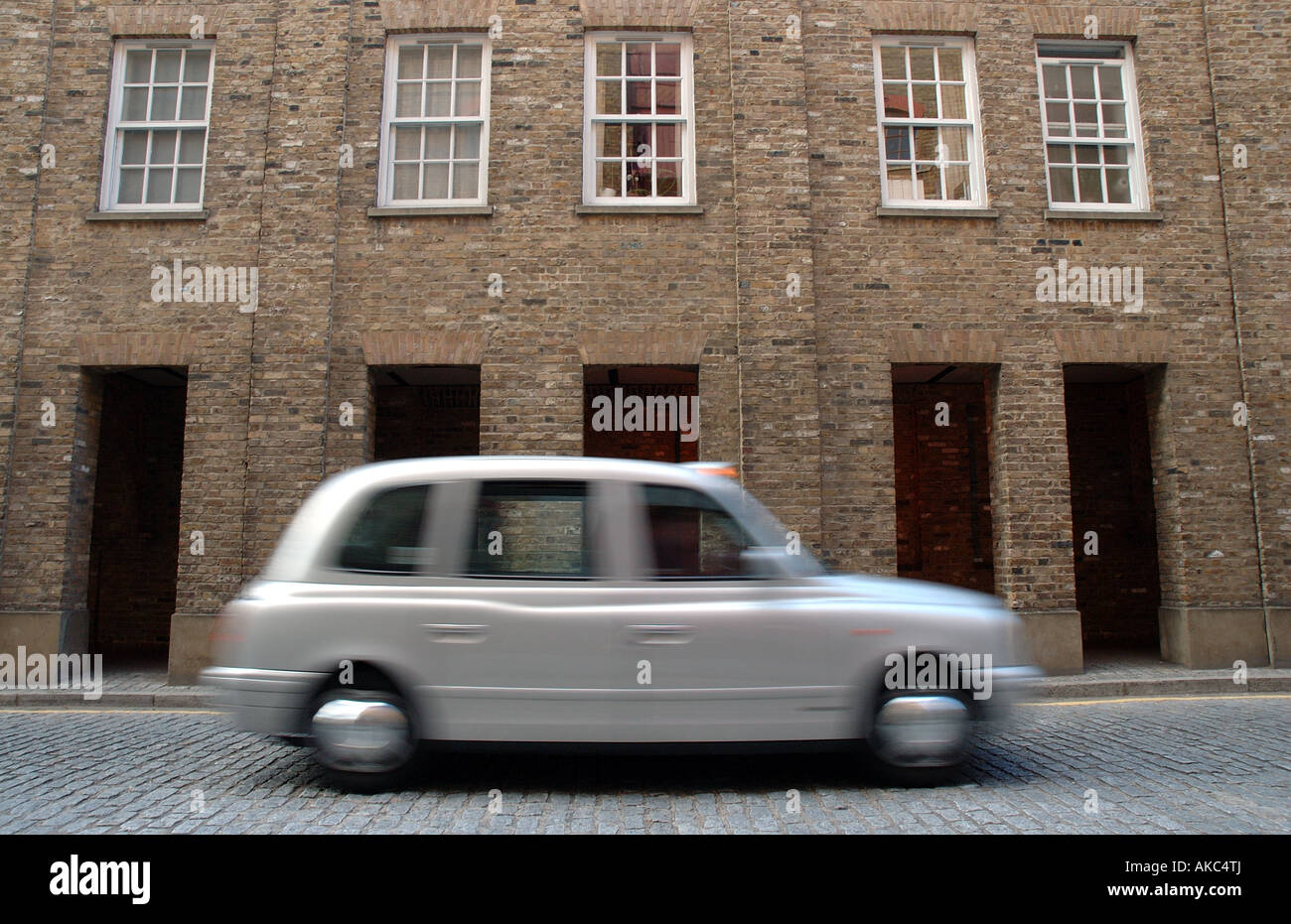 A London icon, a licenced silver taxi rushing through the cobbled streets of Wapping Stock Photo