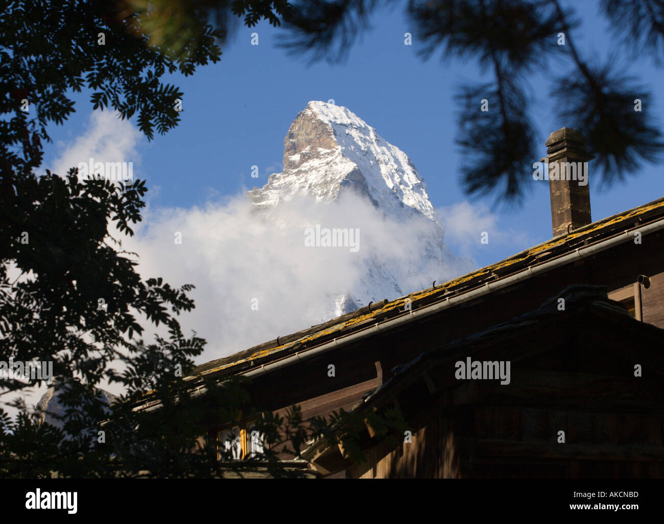 Peak of Matterhorn mountain framed by fir tree branches and chalet roof with chimney viewed from Zermatt Valais Switzerland Stock Photo
