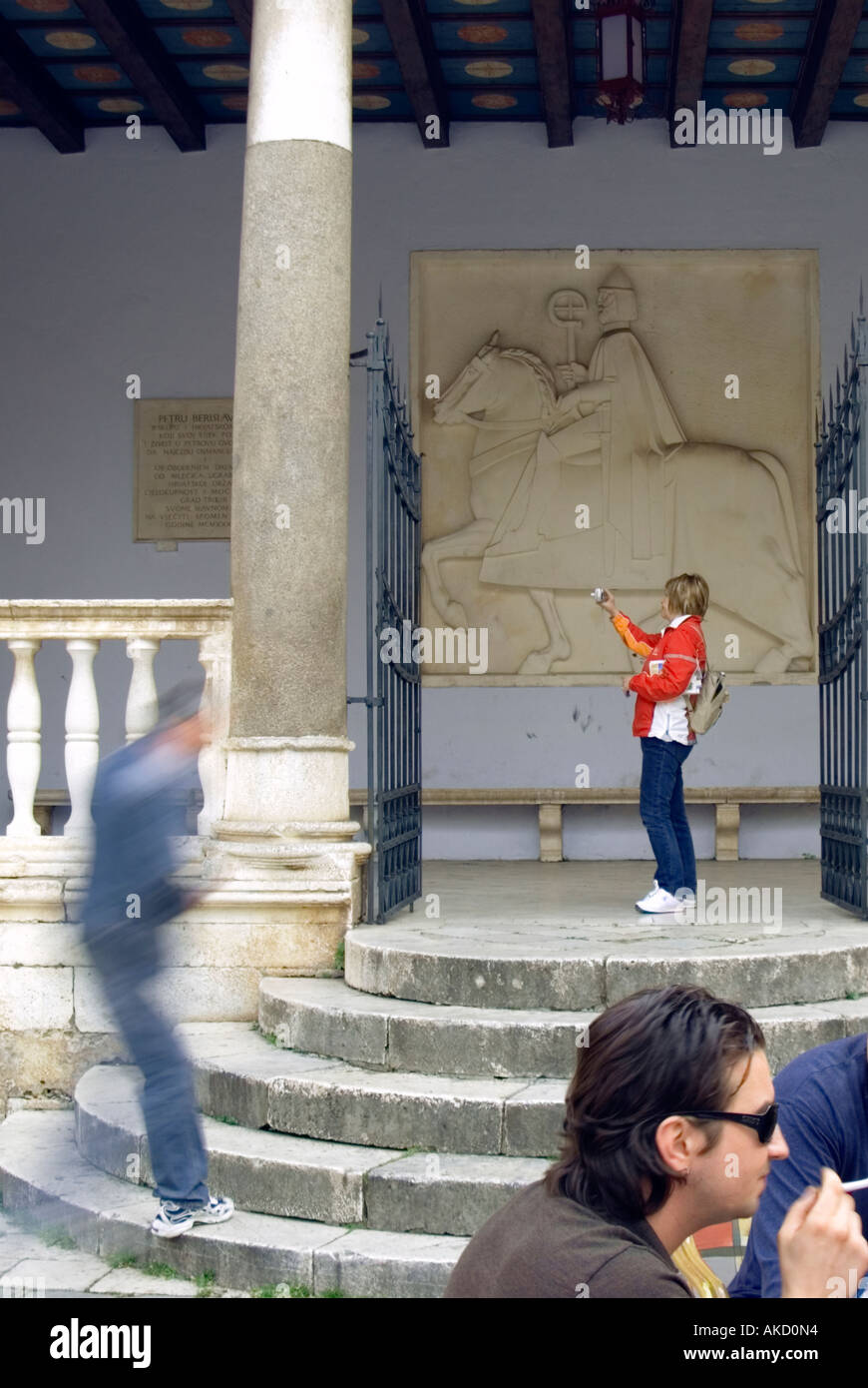 South-East Europe, Croatia, Dalmatia, Trogir, tourist on stone steps photographing metal gate in front of carving Stock Photo