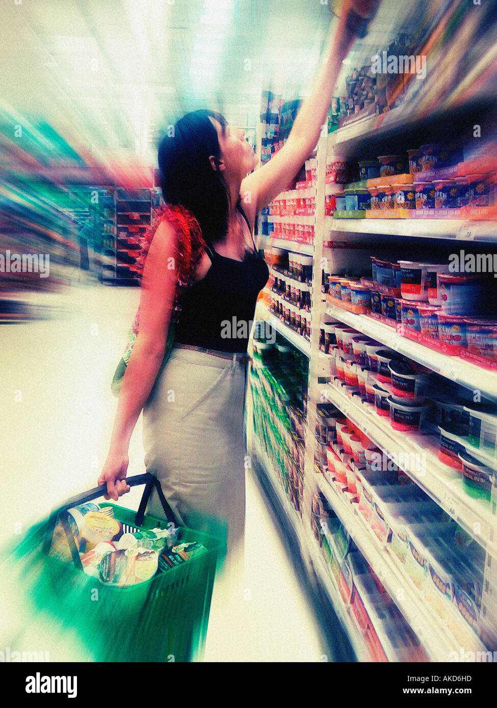 Unidentifiable Caucasian woman carrying a green plastic basket full of shopping in UK Supermarket. Stock Photo