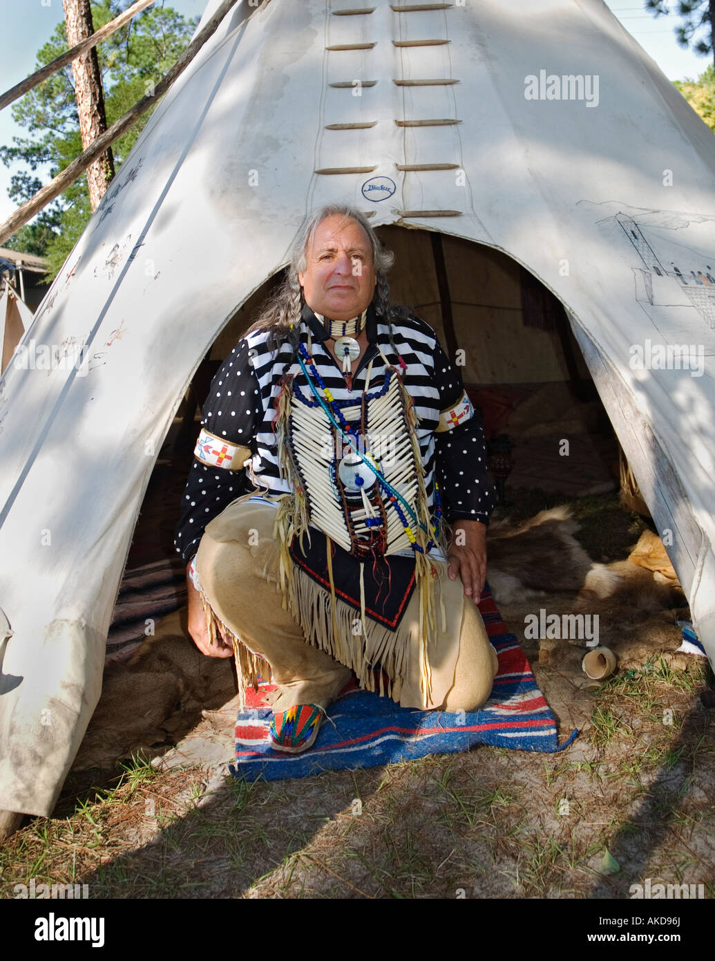 Native American reenactor, Ken Miller, aka Cross Eagle, kneels at entrance to his tepee lodge at Native American festival in Lake City,, Florida. Stock Photo