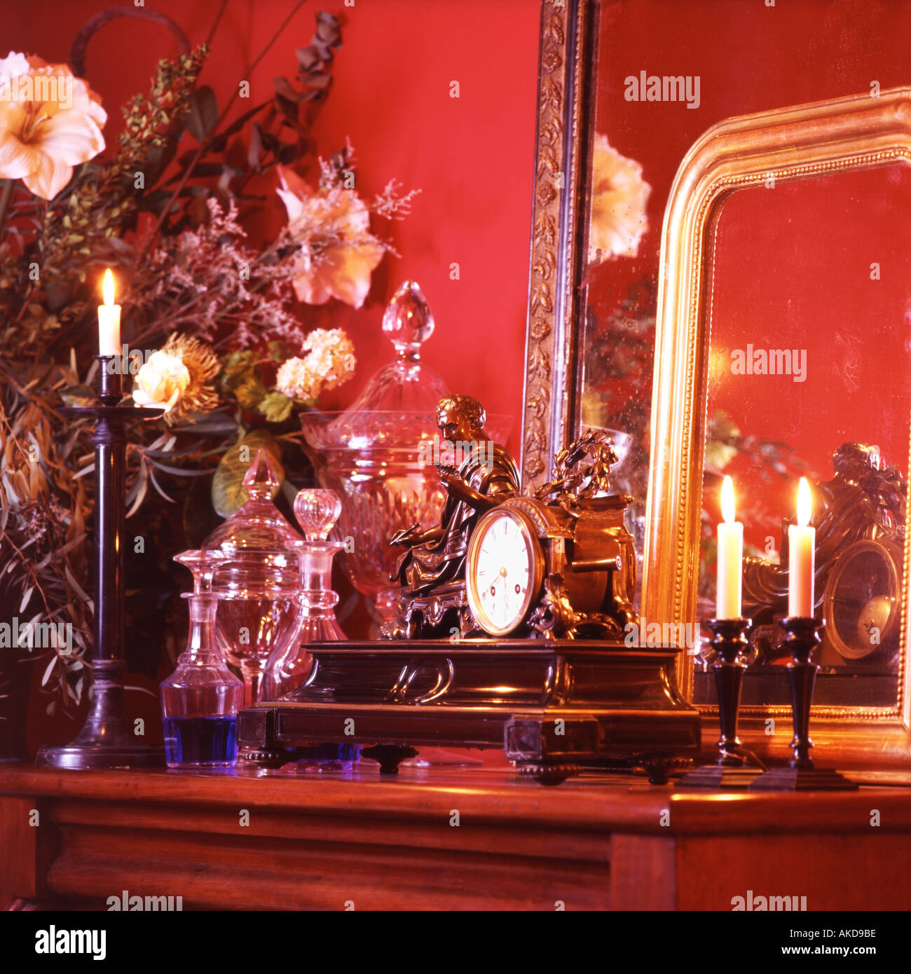 Antique bronze clock with sitting male figure with crystal decanters and flowers and mirrors in front of a red wall Stock Photo