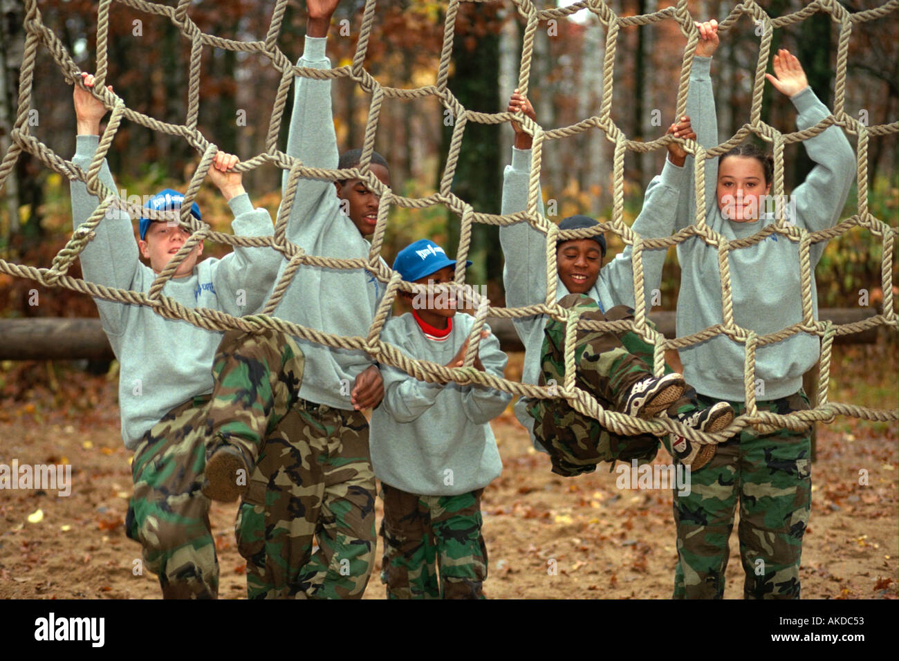 Multiethnic teens age 14 climbing rope net in obstacle course. Camp