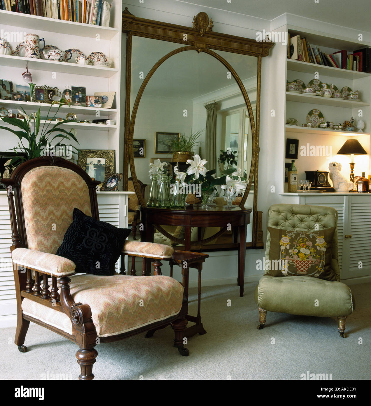 Edwardian armchair and small green Victorian chair on either side of  console table below large antique mirror in living room Stock Photo - Alamy
