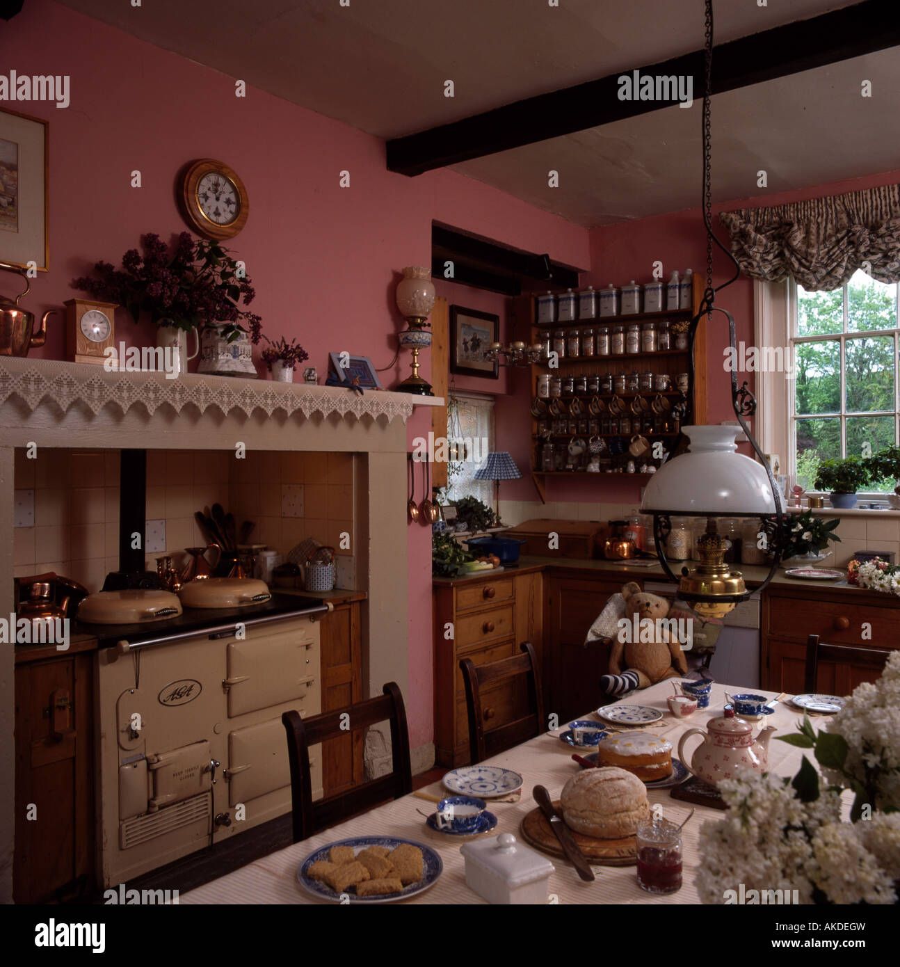 Cream Aga in pink kitchen with table set for tea below Victorian style brass lantern Stock Photo