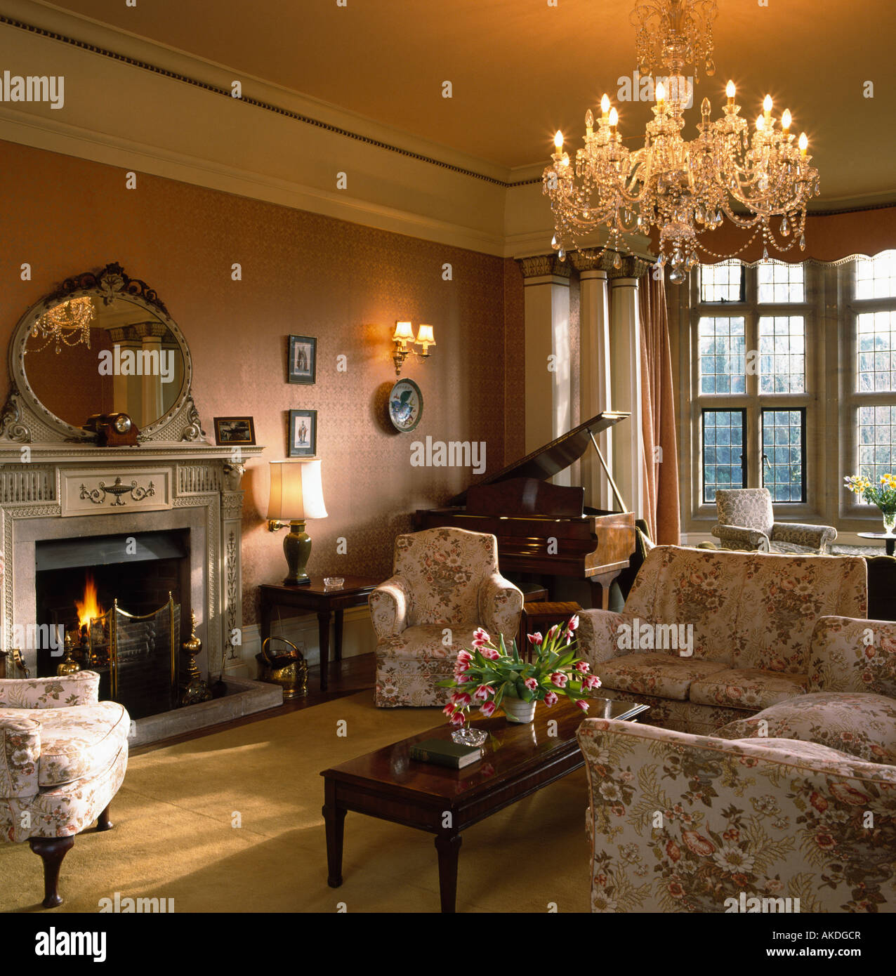 Glass chandelier in country living room with piano in the corner of the  room and lighted fire in fireplace Stock Photo - Alamy