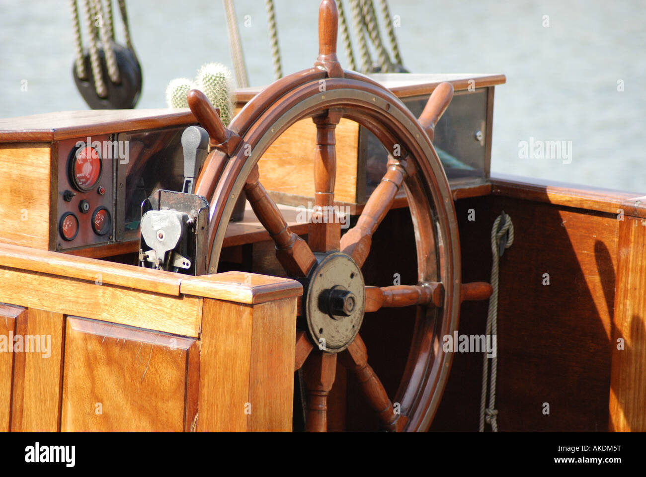 Helm wheel which steers boat moored in a harbour in Hull docks on a sunny day, background includes wood, ropes and shadows. Stock Photo