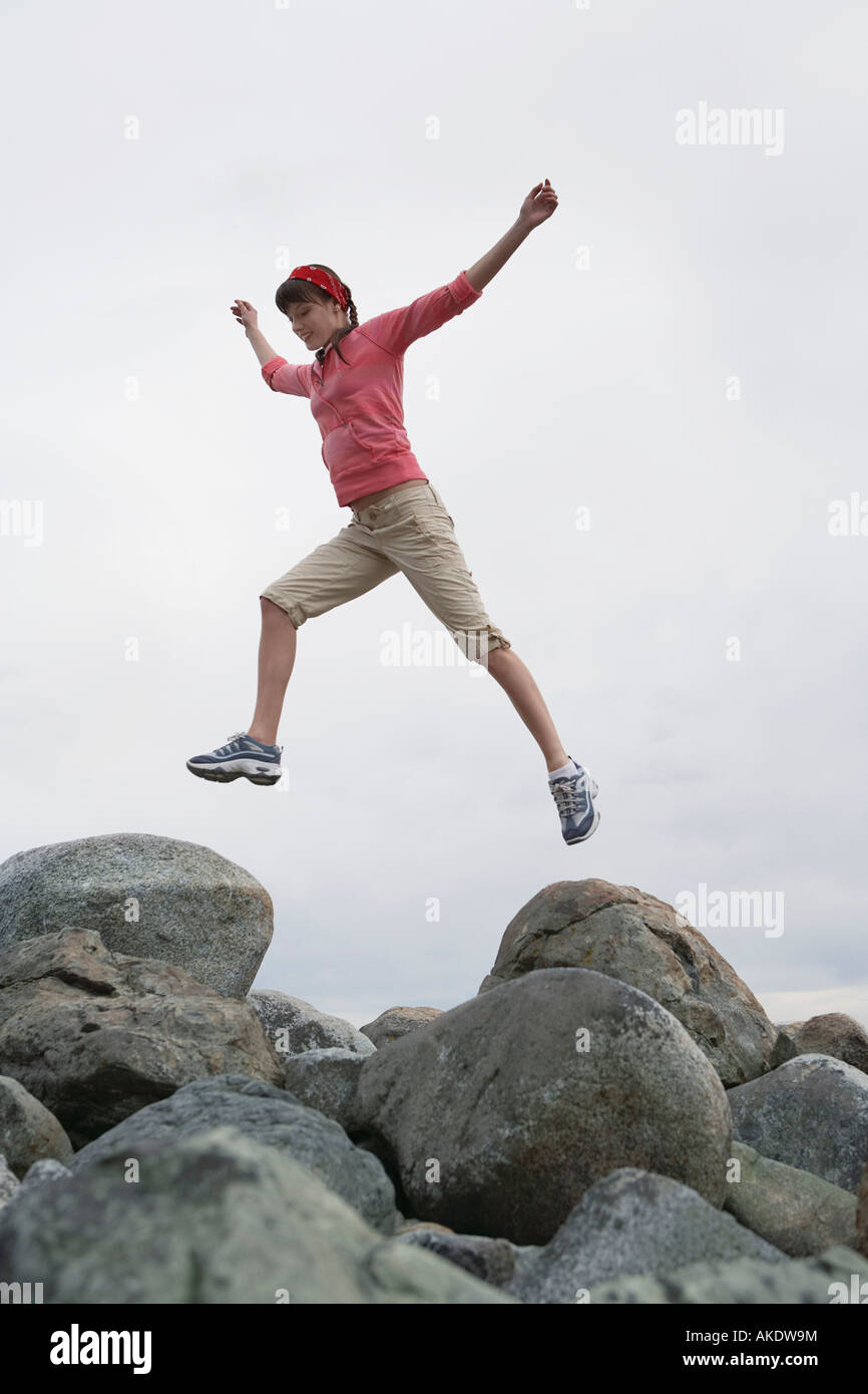 Woman leaping with arms raised over rocks Stock Photo