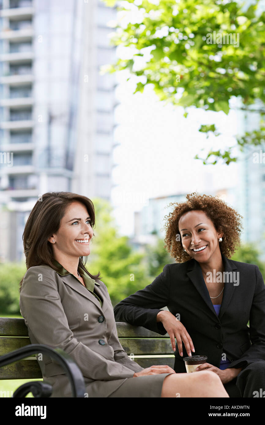 Two business women sitting on park bench, smiling Stock Photo - Alamy
