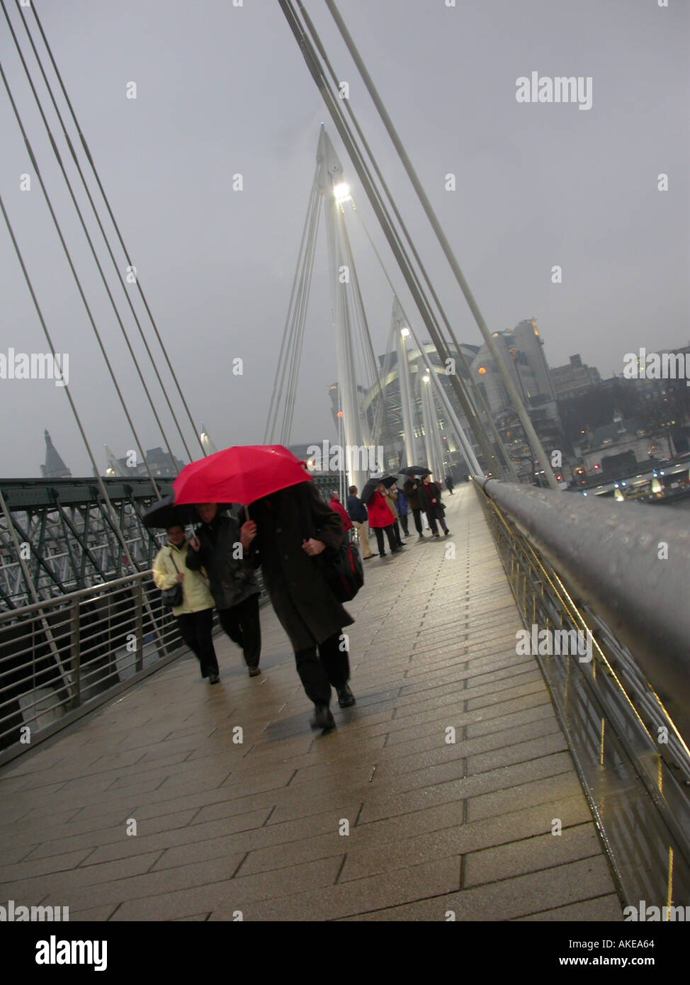 People crossing from Charing Cross station on Hungerford Bridge in rain Stock Photo