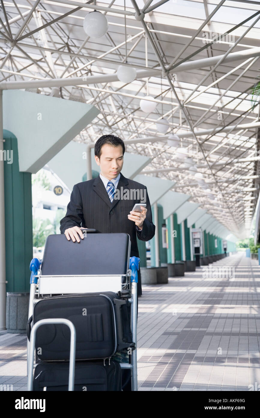 Businessman using a palmtop and pushing a luggage cart Stock Photo