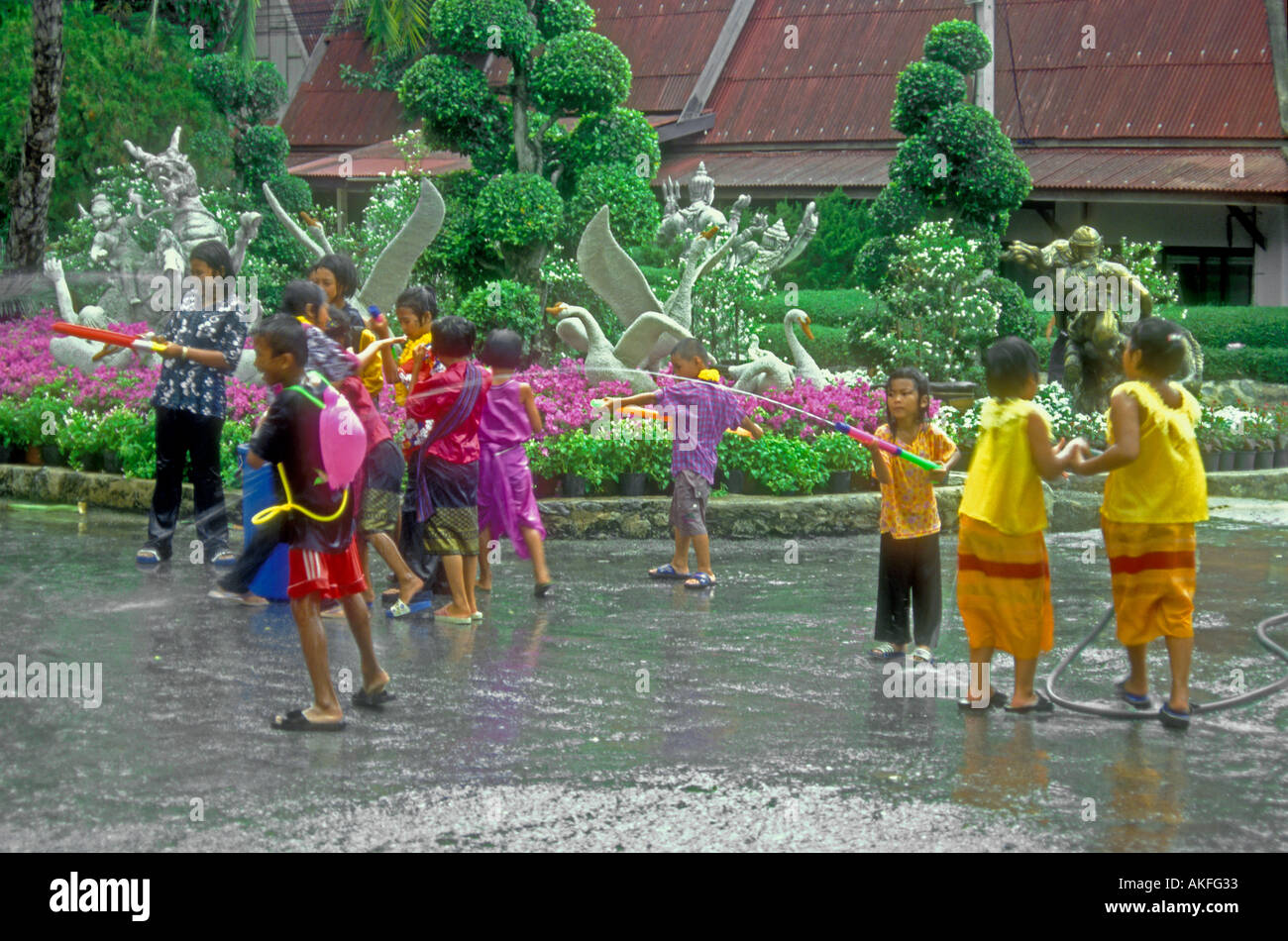 Songkran, children mixed age spraying water with portable water cannons, boy wearing water gun back pack, Nong Nooch Theme Park, Pattaya, Thailand Stock Photo