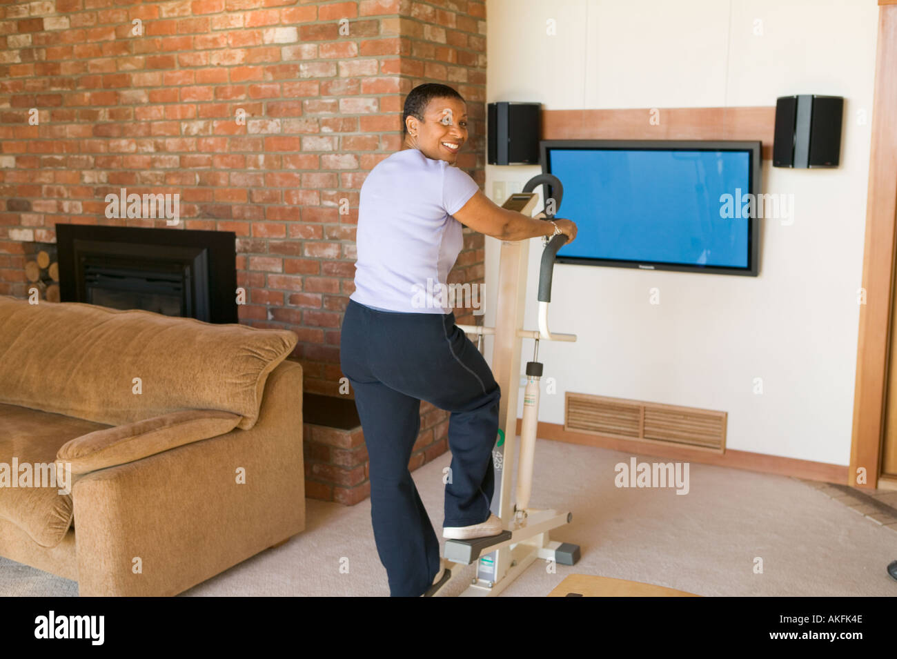 Senior African American exercising on stepper machine and plasma TV Stock Photo