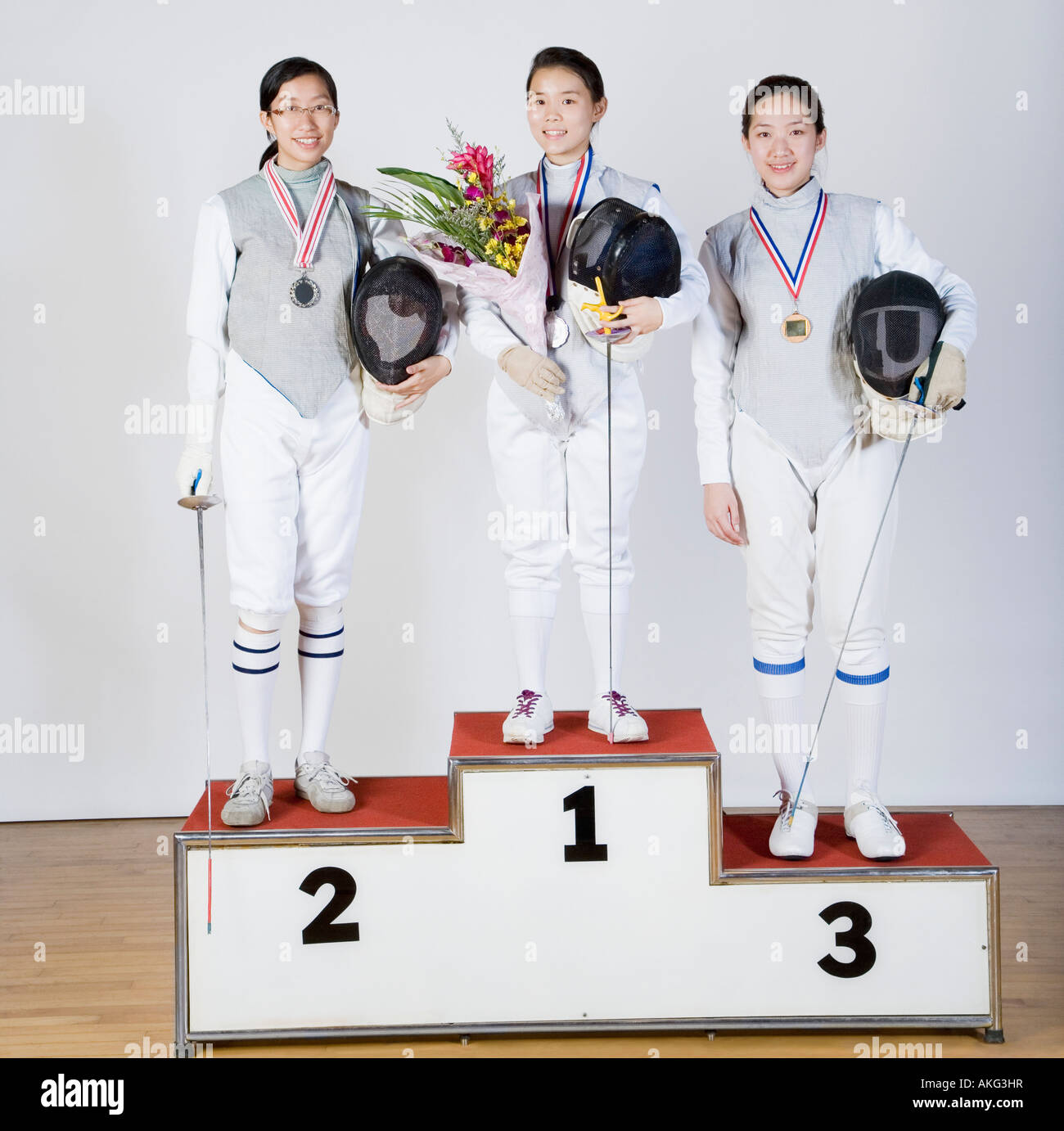 Portrait of three young women in fencing costumes standing on a winner's podium Stock Photo