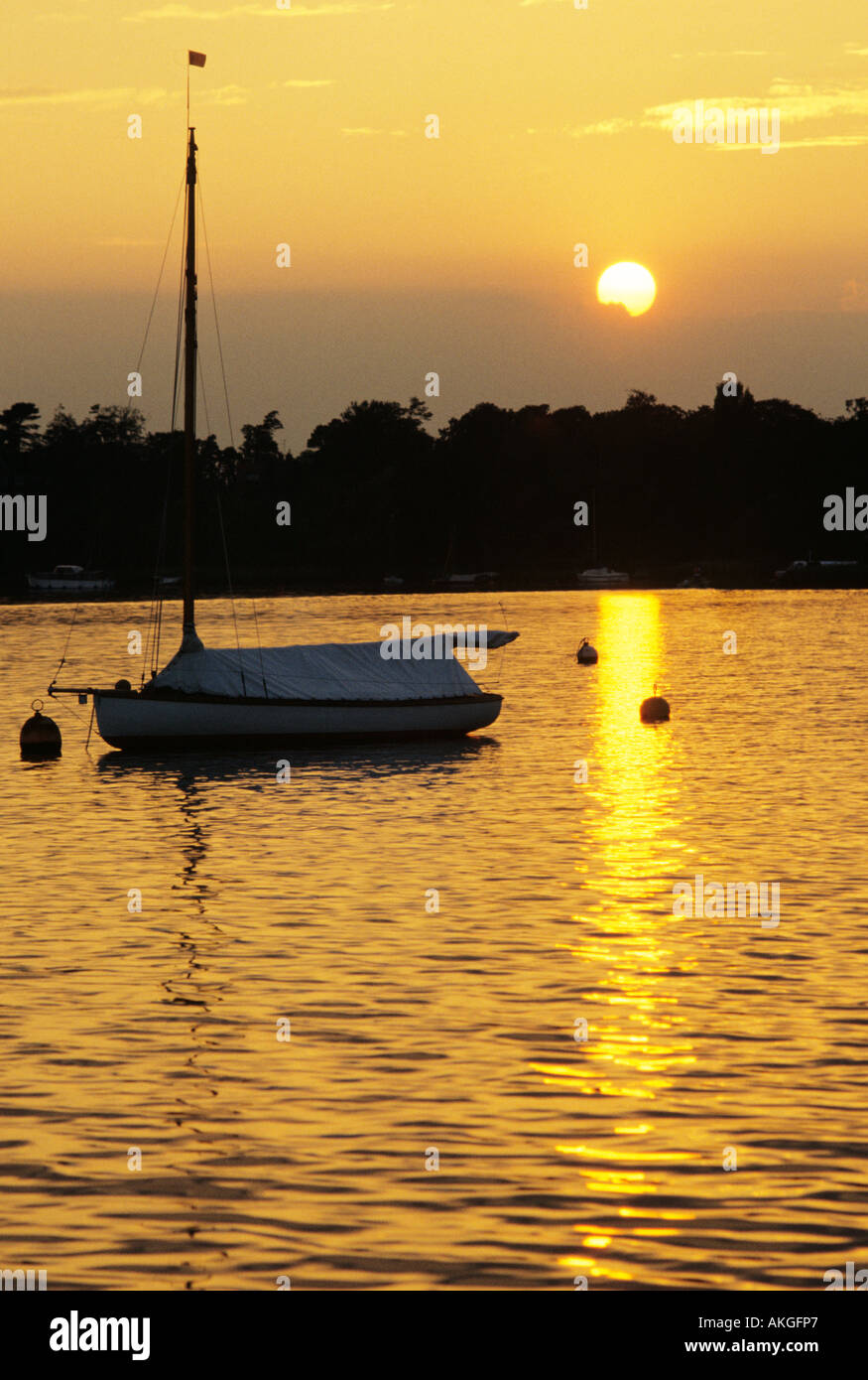 Sunset over water with moored and covered sailing yacht in foreground. Oulton Broad, Suffolk, England Stock Photo