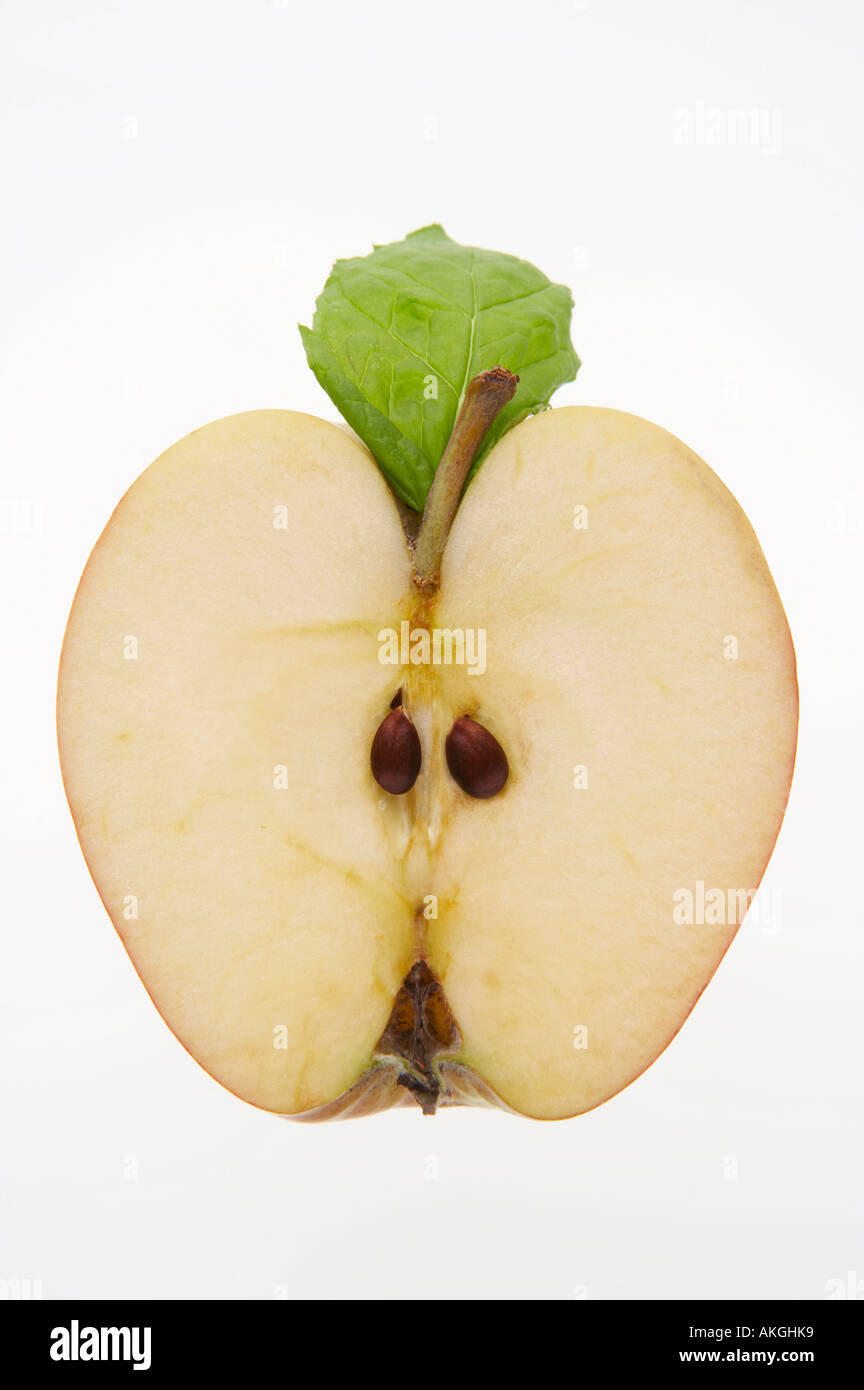 FRESH APPLE WITH GREEN LEAF SLICED IN HALF SHOWING PIPS ON WHITE BACKGROUND Stock Photo