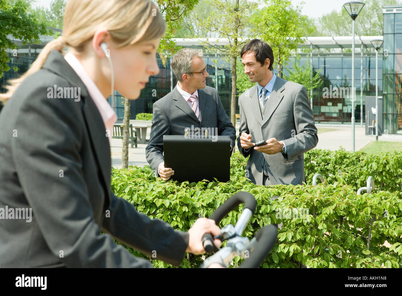 Woman on bike, two businessmen on background Stock Photo