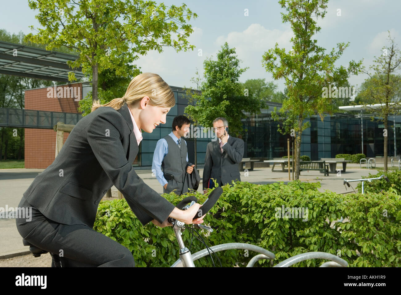 Woman on bike, two businessmen on background Stock Photo