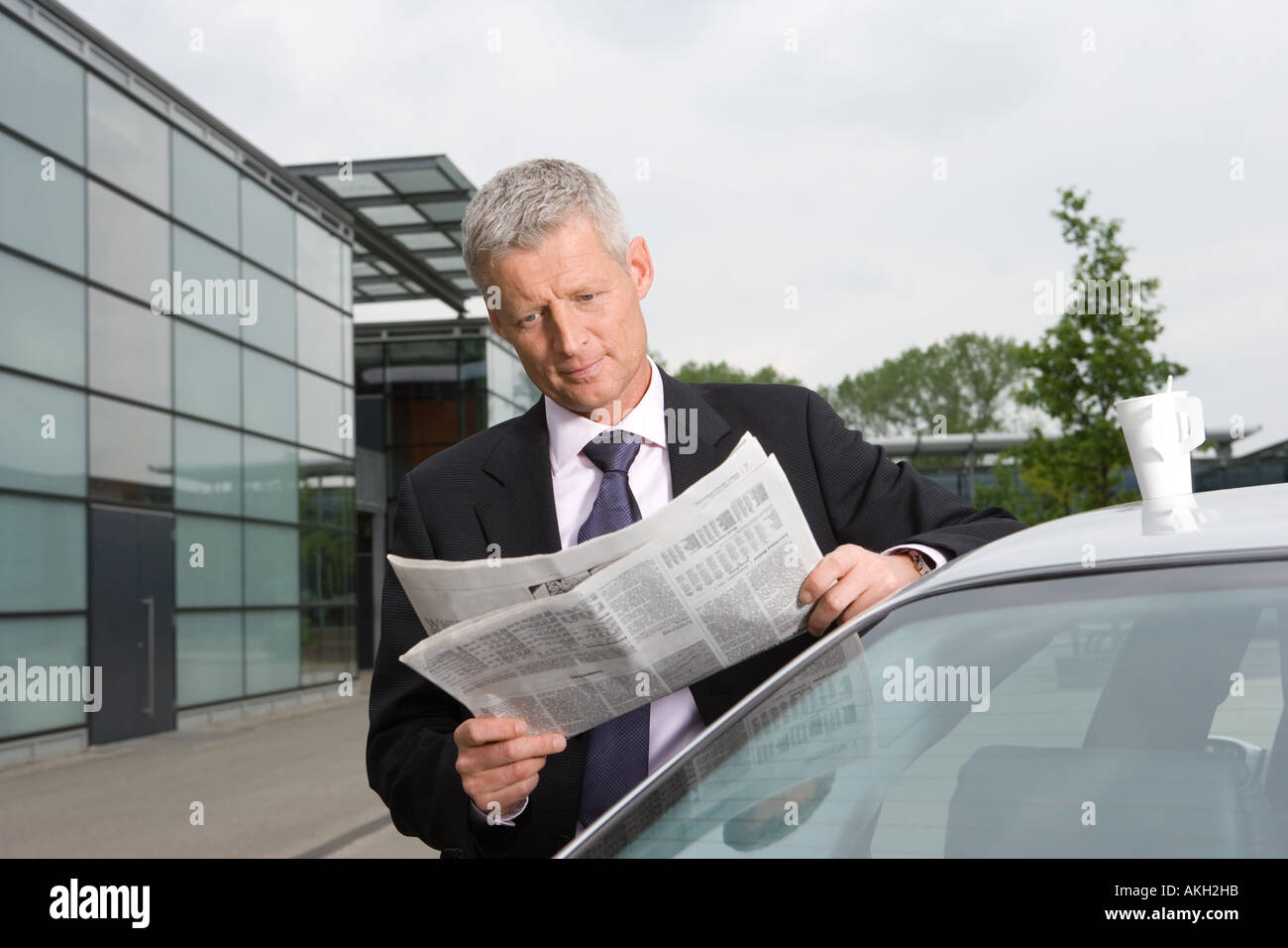 Businessman reading newspaper by car Stock Photo