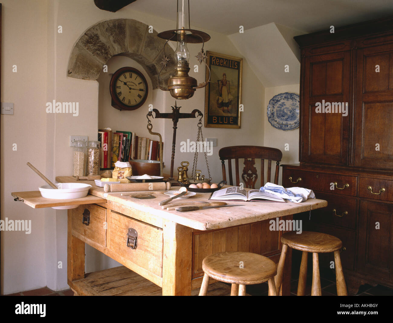 Antique brass scales on Victorian bakers table in country kitchen with clock below stone arch Stock Photo