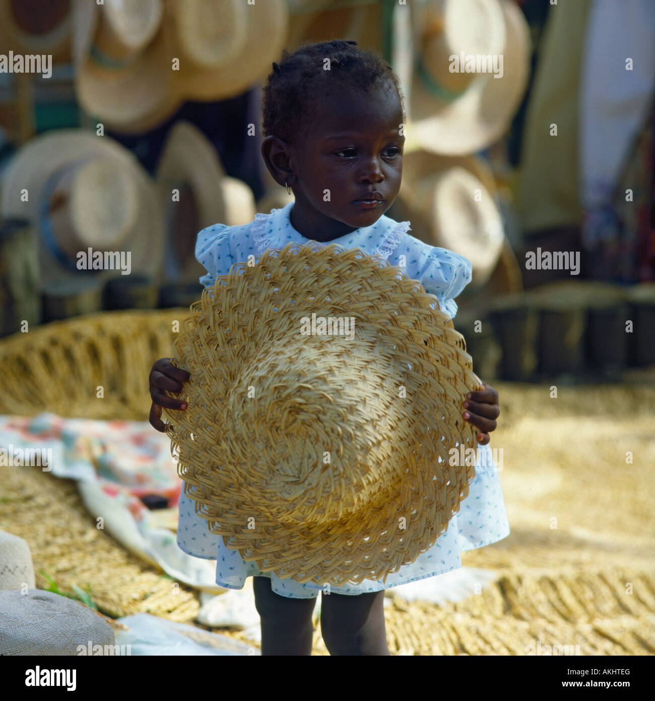 Little girl in pretty spotted dress shyly holding straw sunhat in front of her at a market stall Ocho Rios Jamaica The Caribbean Stock Photo