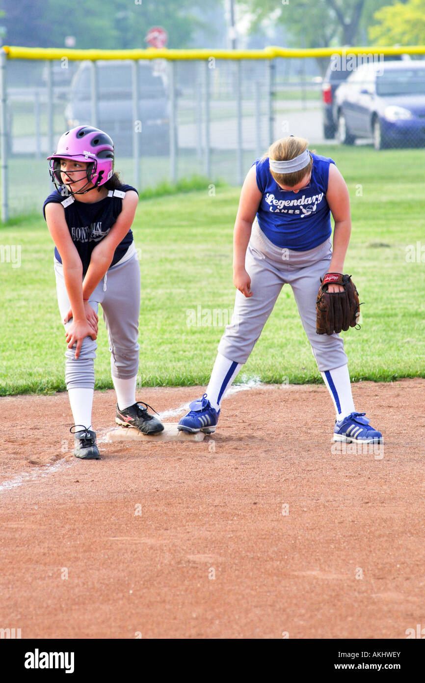 Female softball player waiting to run to third base wearing a pink and black helmet Stock Photo