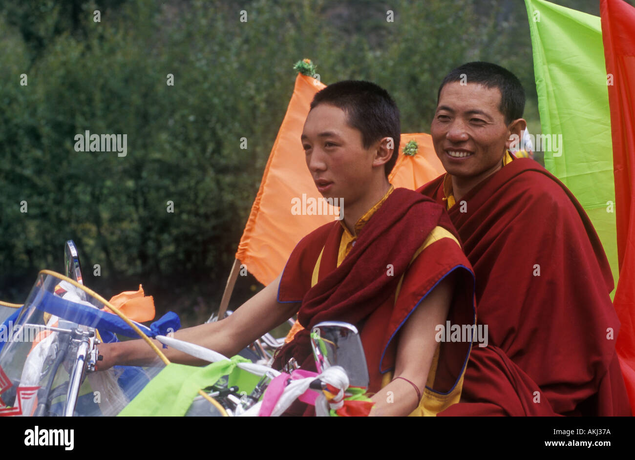 Buddhist monks with motorcycle decorated with katoks and prayer flags Kham E Tibet Sichuan Province China Stock Photo