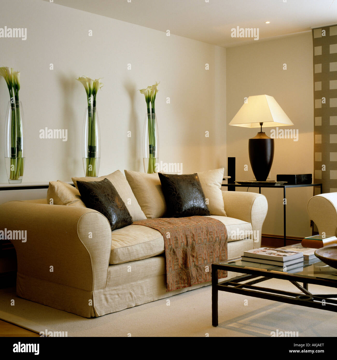 Living room with sofa, glasstopped coffee table and lily stems in