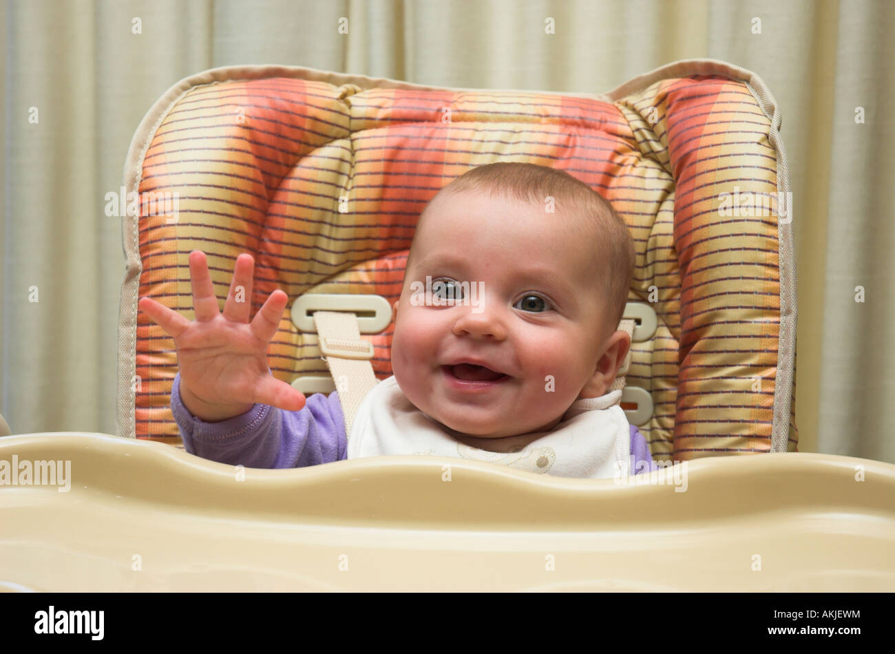 A six month old baby sitting in a high chair ready for meal time Stock