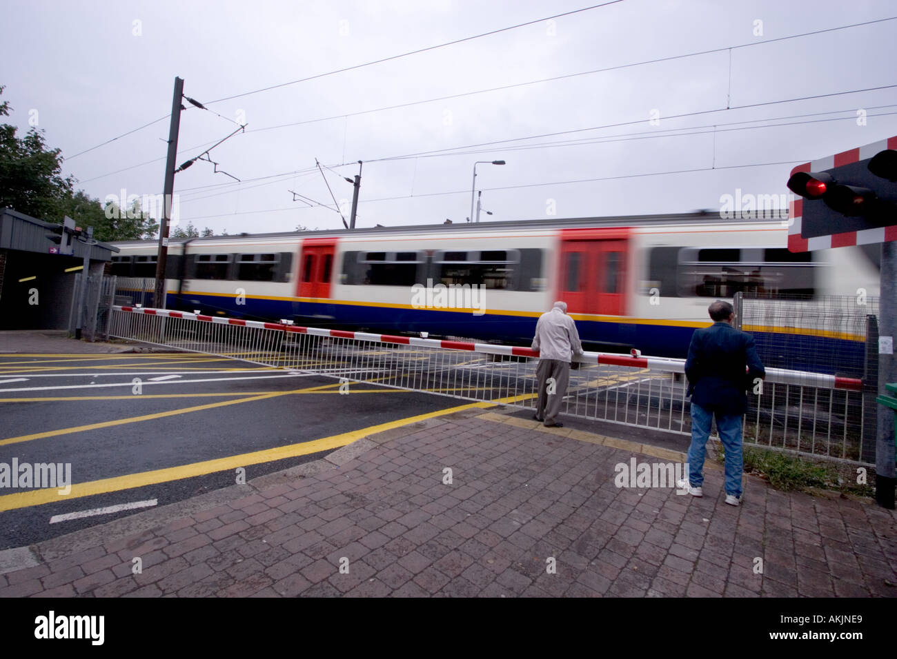 Level crossing with barriers and flashing lights and man leaning on barrier Highams Park London