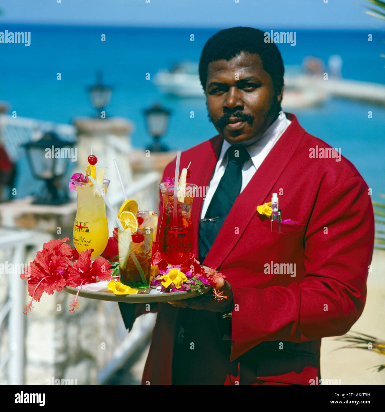 Local male waiter in red coat white shirt and tie holding tray of