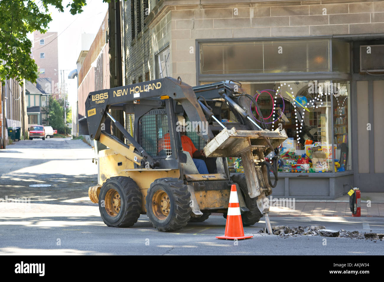 WORKERS Evanston Illinois Man use jackhammer on bobcat to repair section of street orange cone urban retail area Stock Photo
