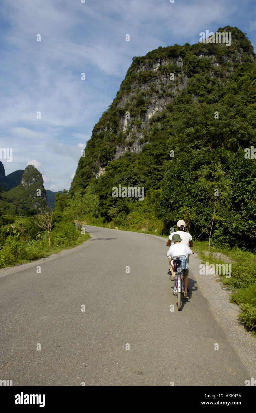 Young Chinese man riding in tandem with a European boy along foliage covered cliffs, Yangshuo, Guangxi, China. Stock Photo
