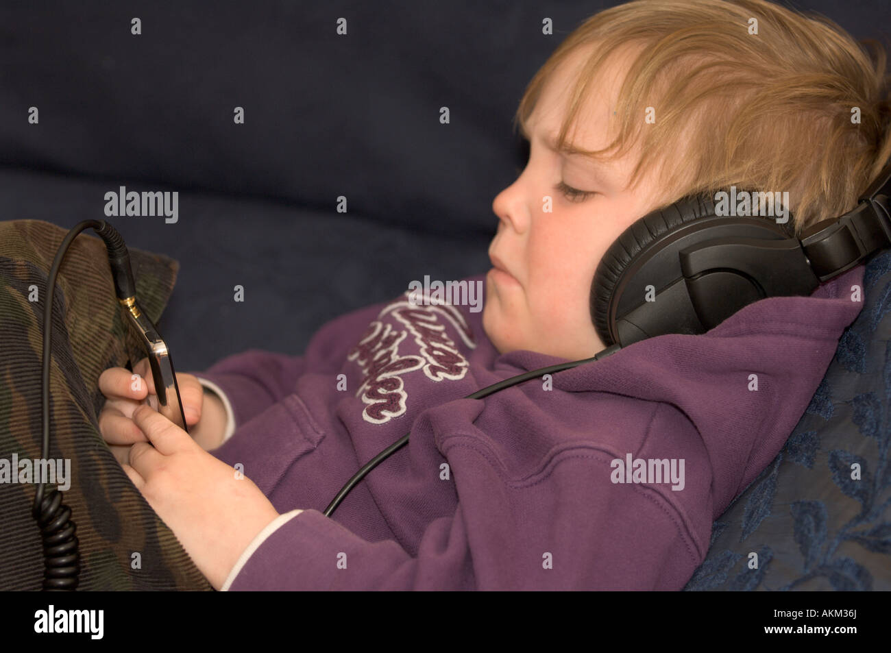 Young child engrossed in watching and listening to a movie (film) via large headphones on a compact mp3 player Stock Photo
