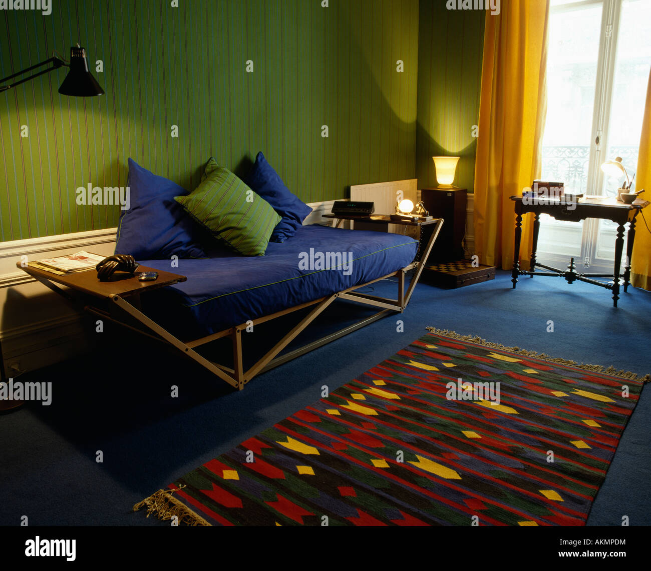 Angular wooden framed blue sofa with green cushions and wallpaper in