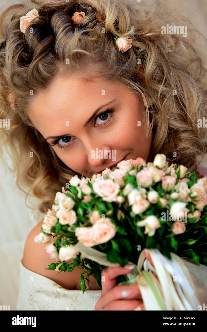 A beautiful blonde bride seen here in a wedding dress smelling her bouquet of flowers on her wedding day Stock Photo