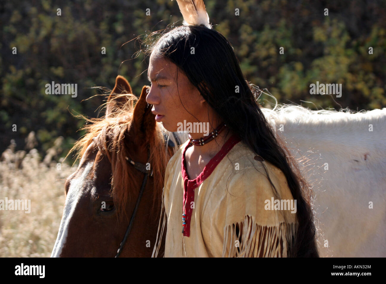 A Native American Indian boy wearing a feather standing next to a horse Stock Photo