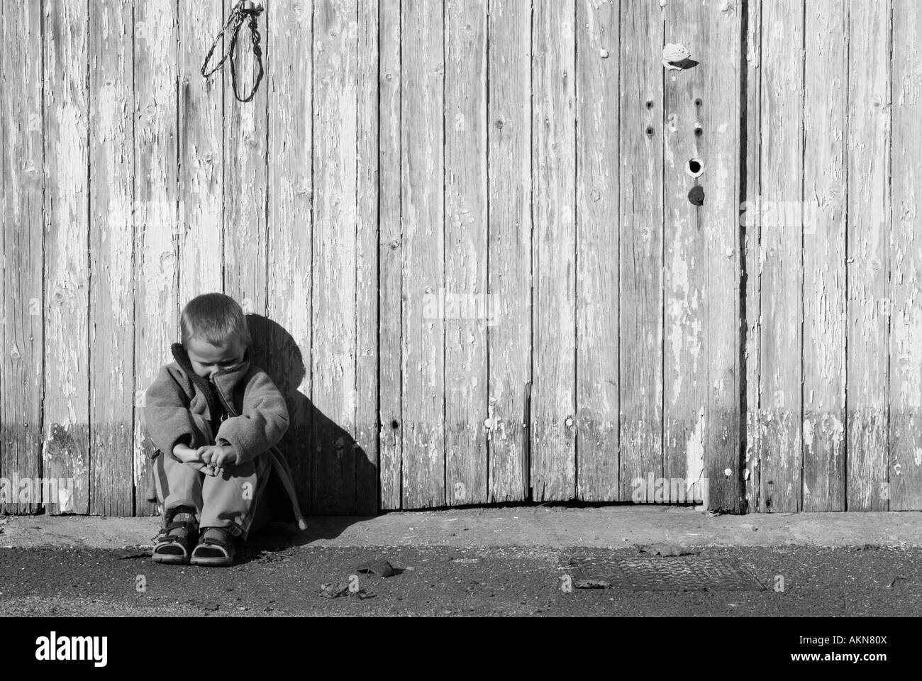 Stock Photo of a Young boy sitting with his head bowed in front of a wooden door Stock Photo Alamy