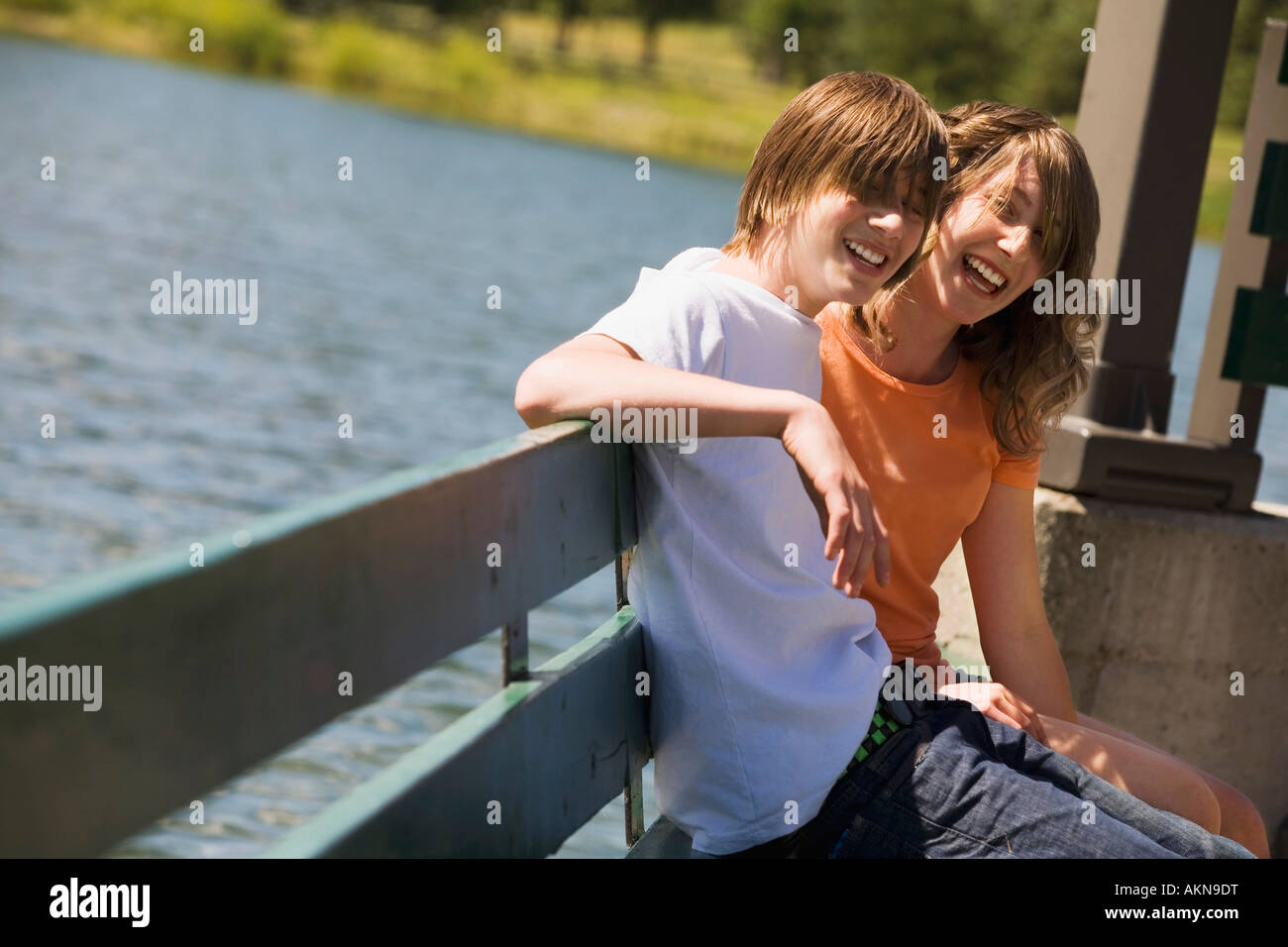 Teenagers sitting on a bench by water Stock Photo