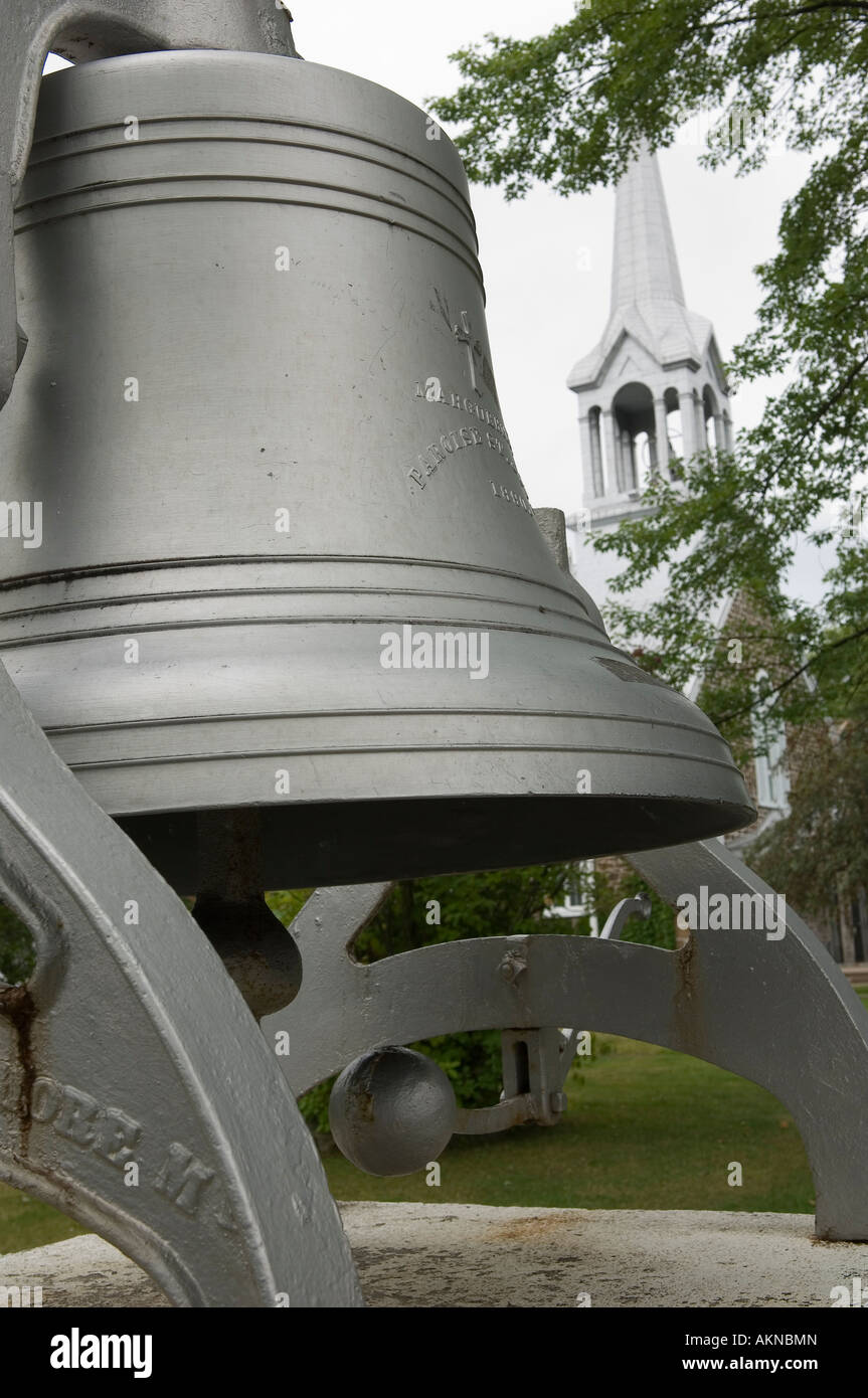 The old church bell with the church spire in the background St Jovite Mont Tremblant Laurentians Quebec Canada Stock Photo