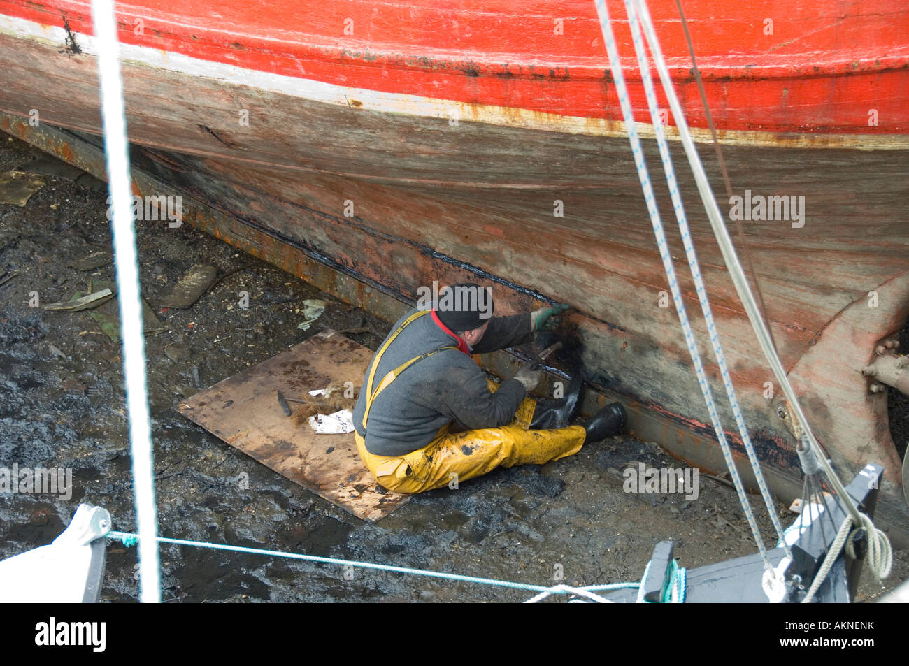 A fisherman repairing the caulking of a fishing boat while the tide is