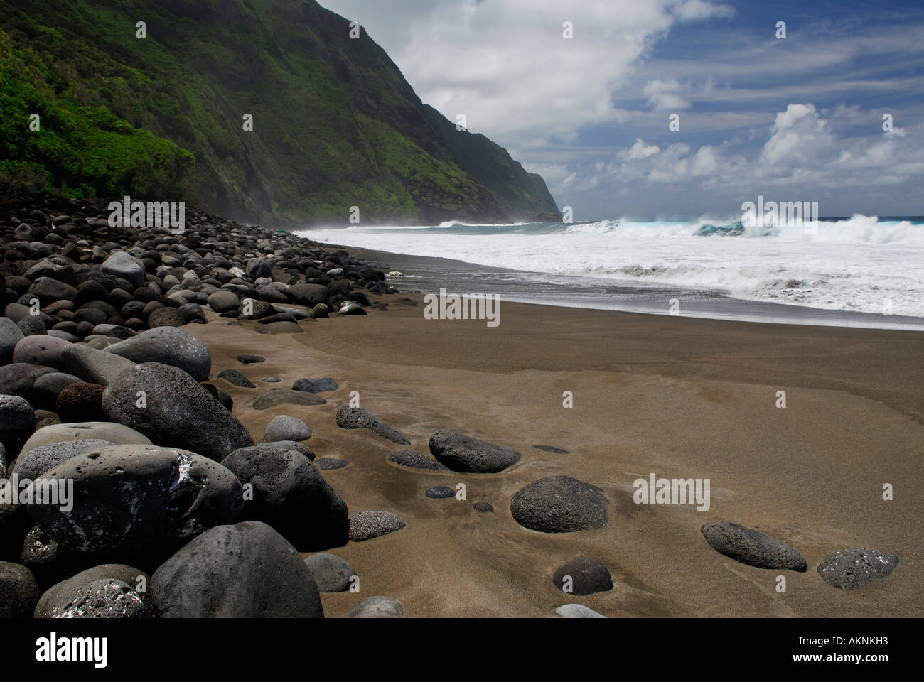 Black sand beach and Steep sea cliffs at Kalaupapa leper colony with smooth lava boulders Molokai Island Hawaii Stock Photo