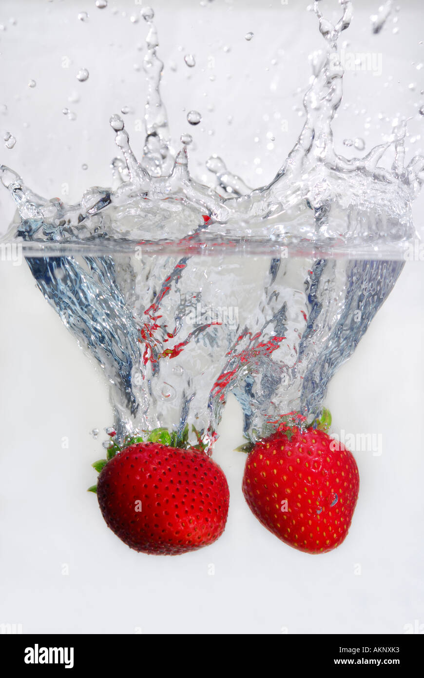 Splashing pair of strawberries dropped into water on white background Stock Photo