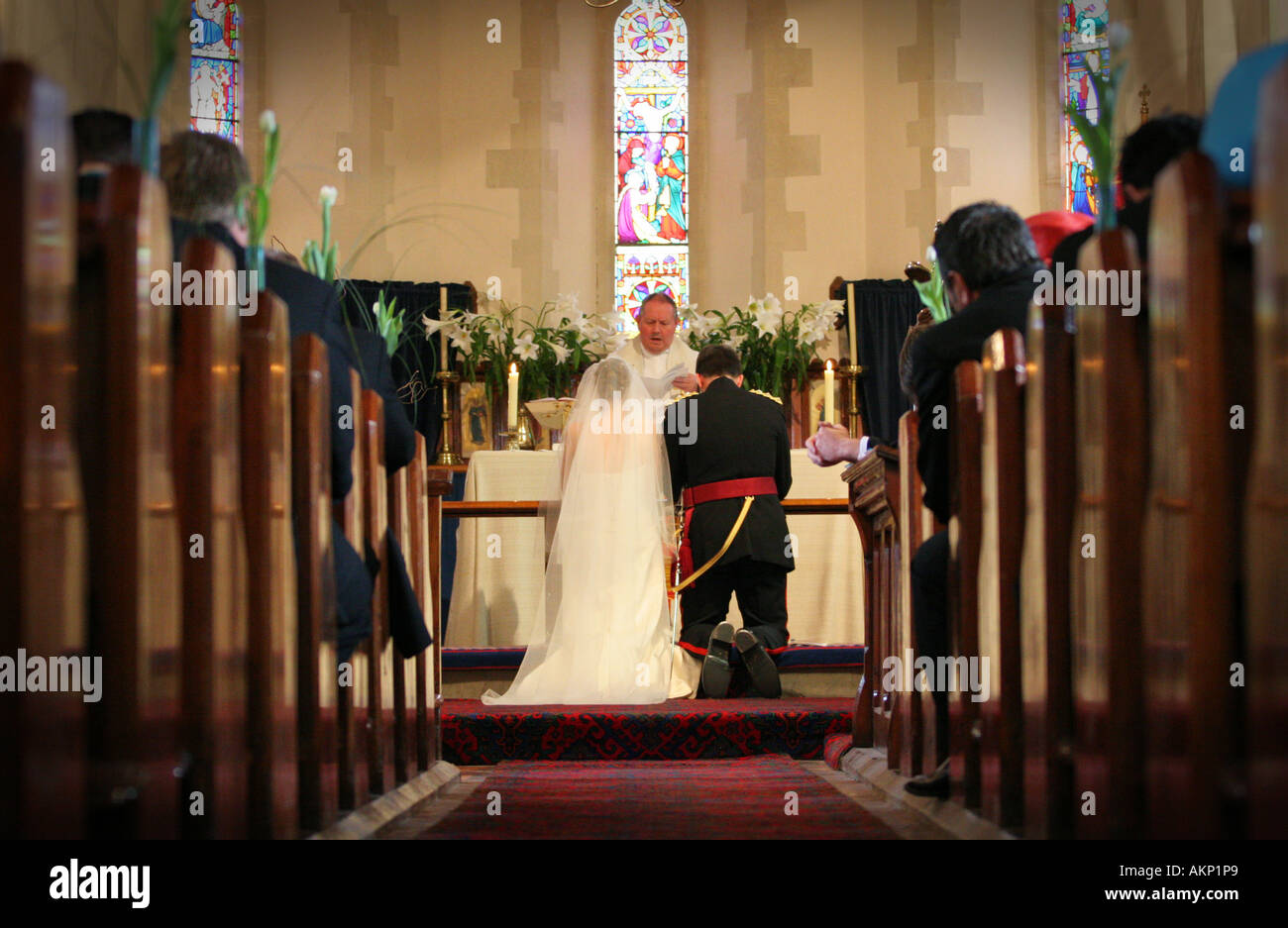 Bride and groom kneel at altar during typical catholic wedding ceremony in ancient village church Stock Photo