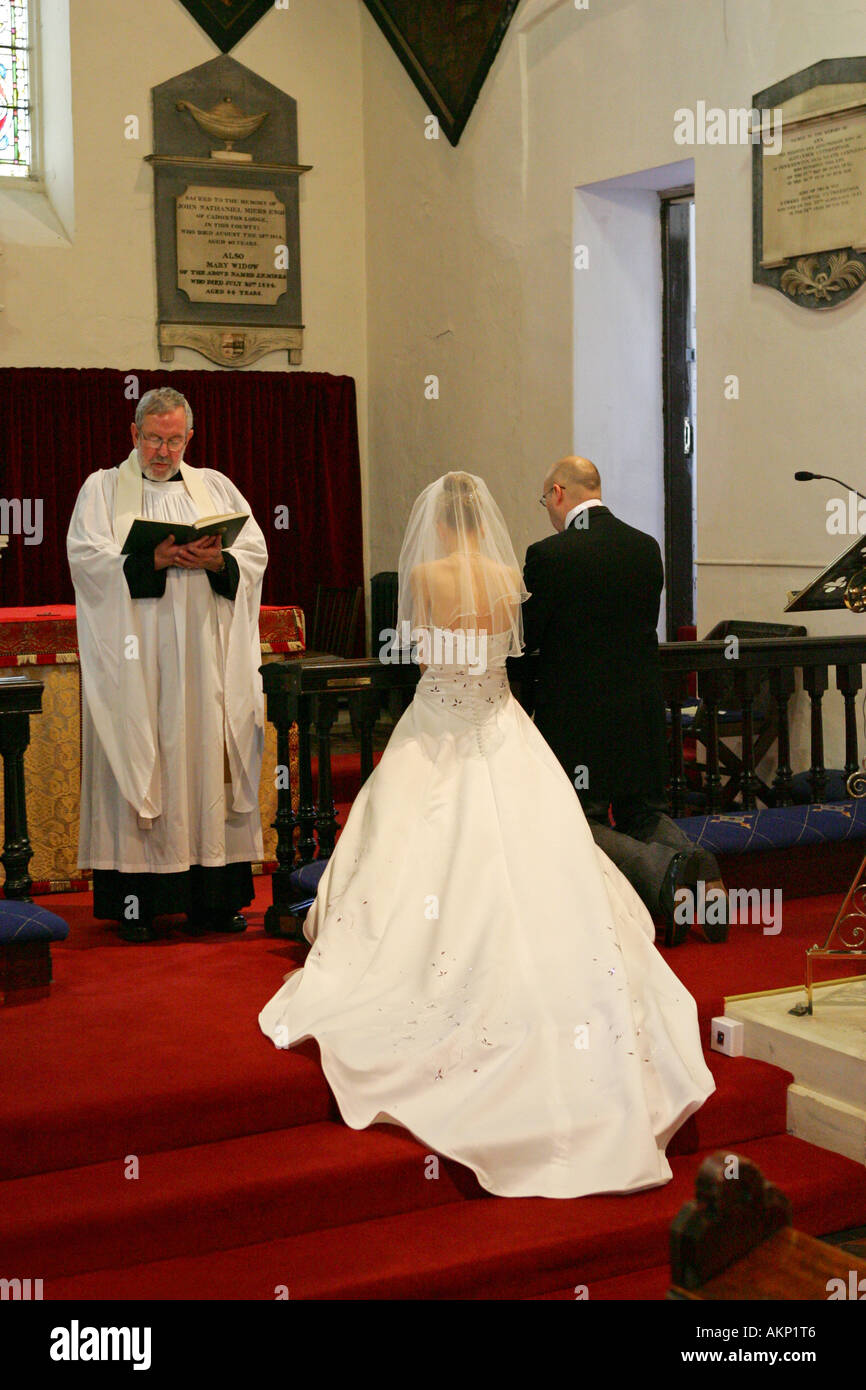 Bride and Groom stand before a priest vicar at the altar during their wedding ceremony with long flowing dress Stock Photo