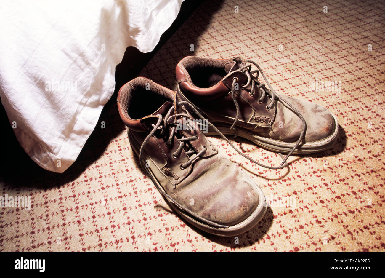 Pair of very dusty leather hiking boots with shoe lases undone on the carpet next to a bed Stock Photo