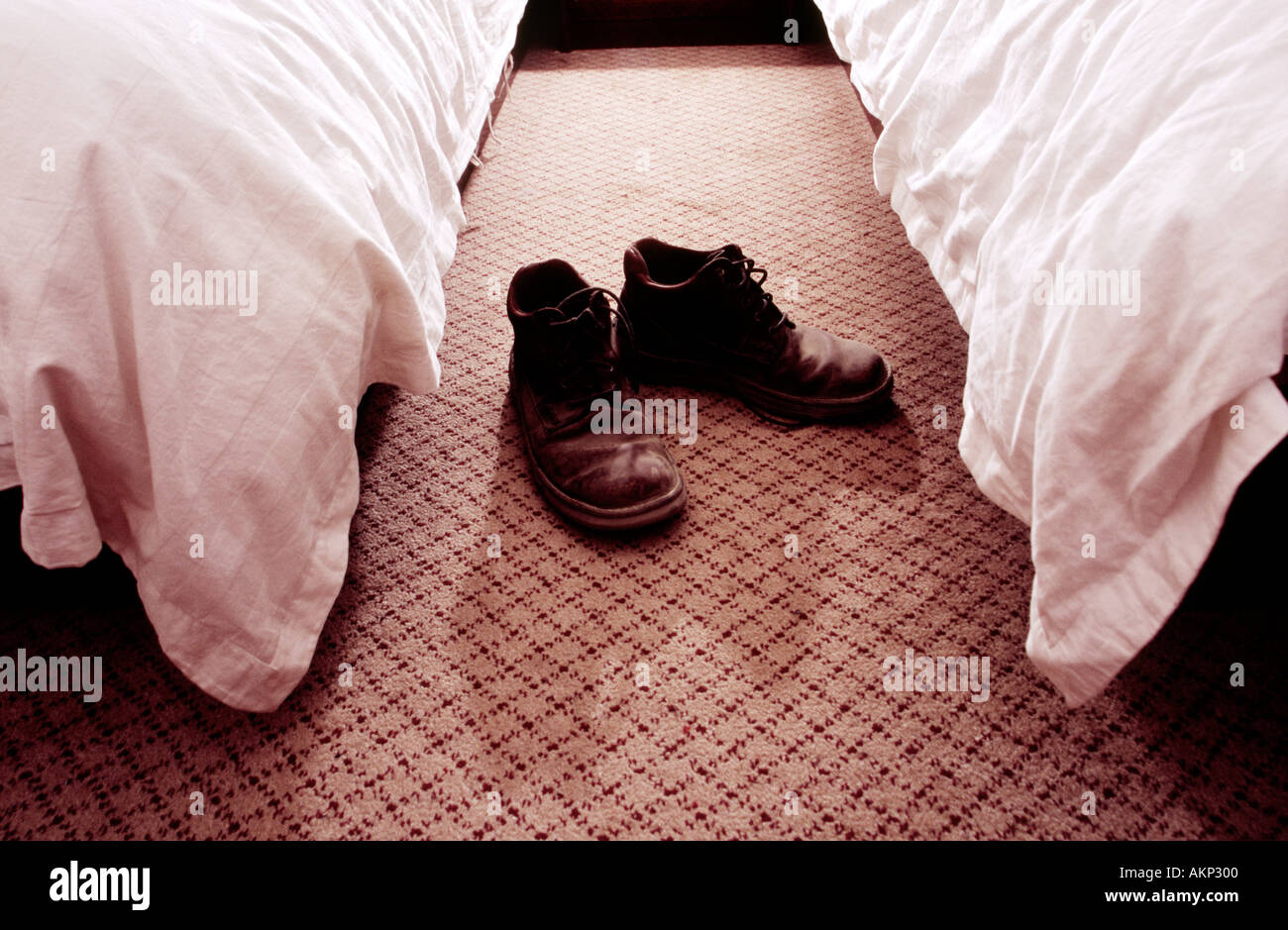 Pair of very dusty leather hiking boots with shoe lases undone on the carpet between two hotel beds Stock Photo