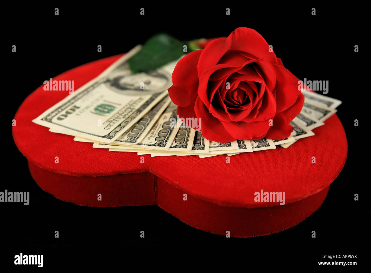 One Hundred dollar bills on red velvet Valentine heart with red rose isolated on black Stock Photo